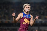 A Brisbane Lions AFL player grins with his tongue out as he celebrates during a game.