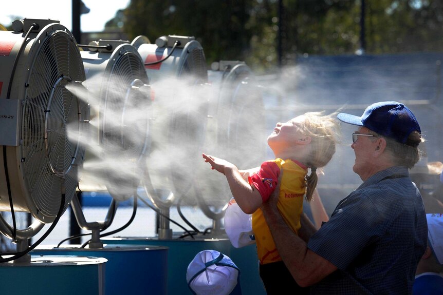 A little girl is held up to enjoy the misting fan