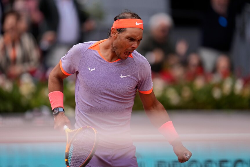 Spanish tennis star Rafael Nadal, in a purple shirt and orange headband, pumps his first after winning a point