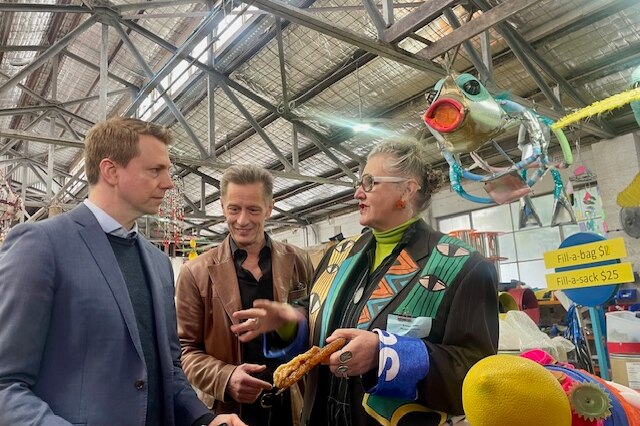 Two men and an older woman ineract with one another at a warehouse filled with recycled goods