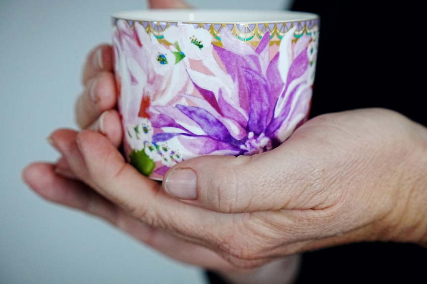 Hands holding a mug with purple flowers.