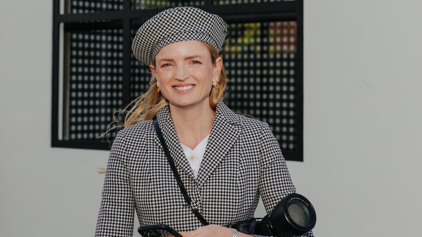 A young blonde woman smiling in a matching houndstooth beret and blazer. 