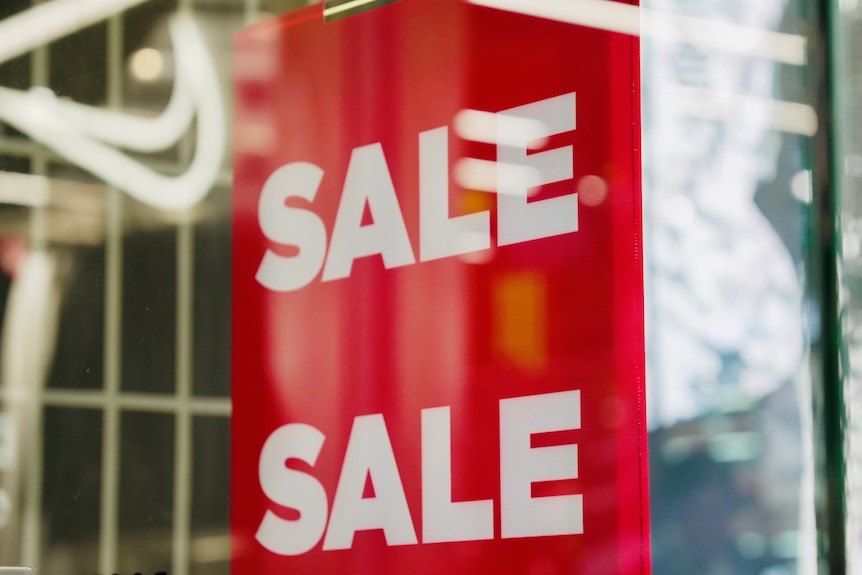 A red sign with white block letters that read "Sale" in a shop front window.