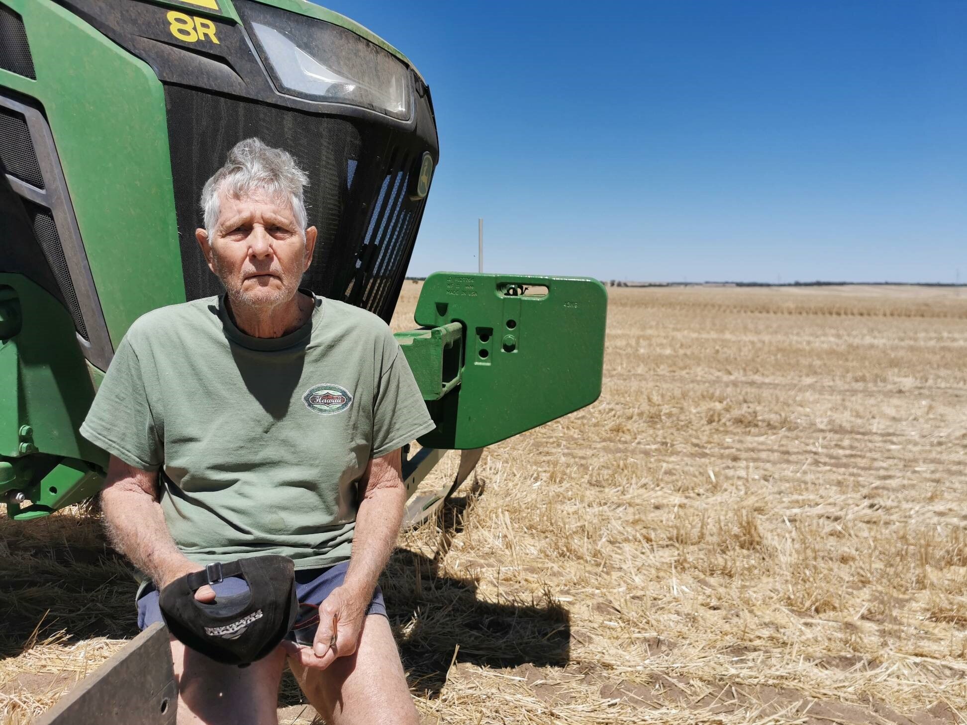 An older fellow stands in a paddock near some farm machinery.