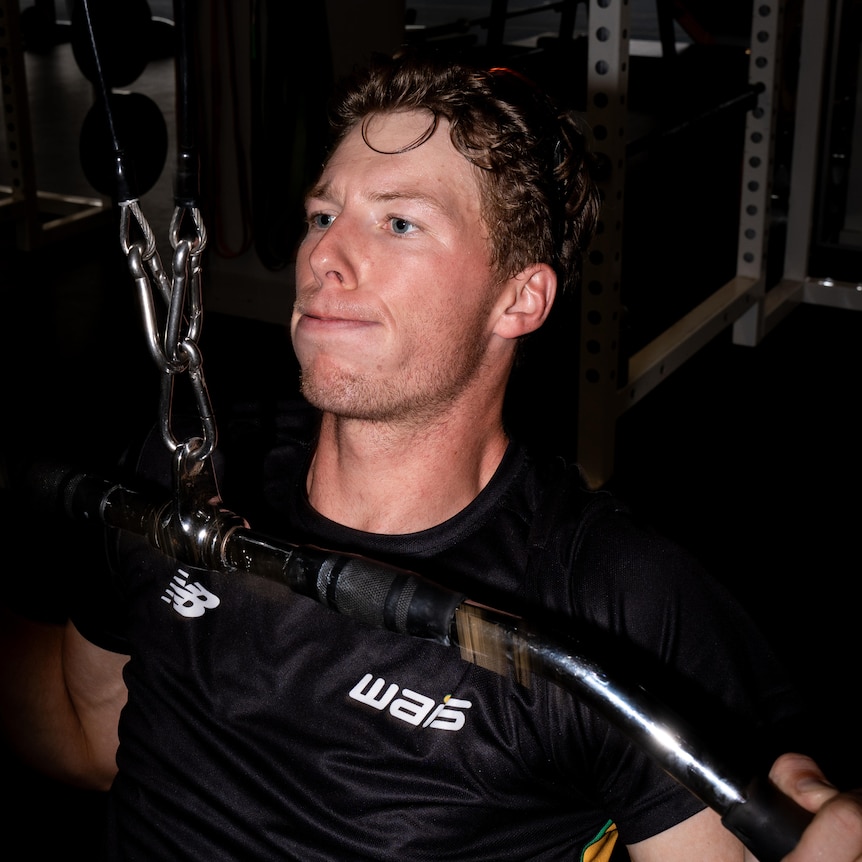 A close-up shot of Riley Rees-Turner lifting weights and wearing a black WAIS shirt.