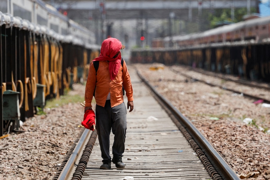 A man covers his face using a cloth to shield himself from the sun as he inspects railway tracks 