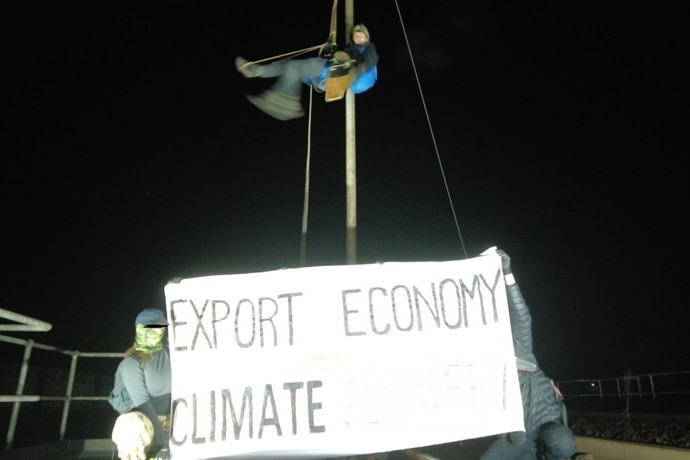 Two people atop a rail bridge protesting coal, holding a sign 