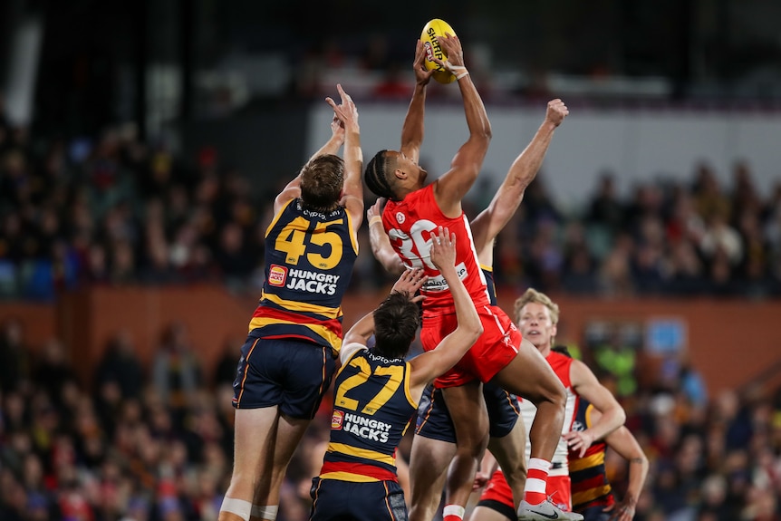 A Sydney Swans player rises and reaches up to grab the ball out of a pack during a game against Adelaide.