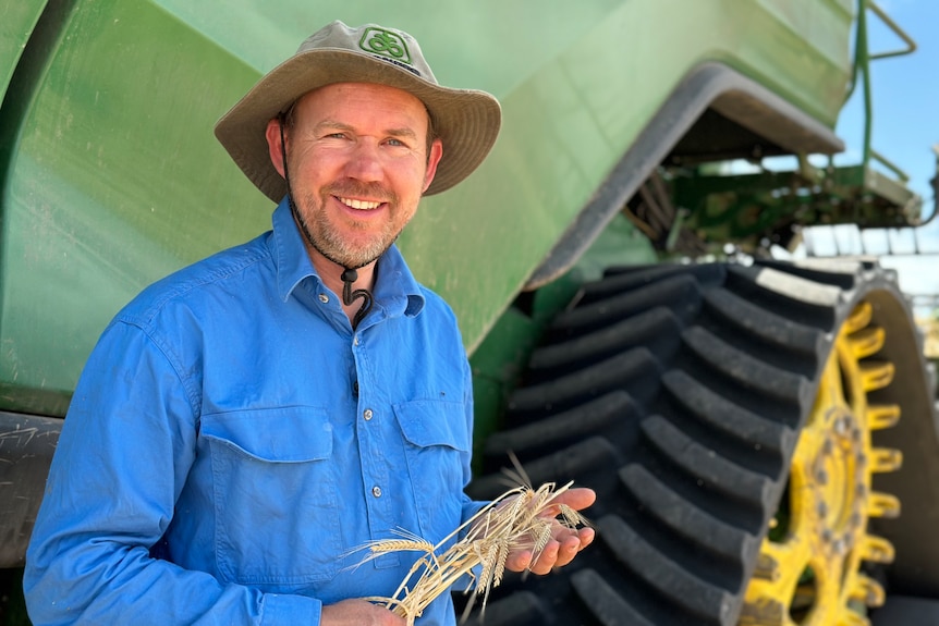 man standing in front of tractor holding barley