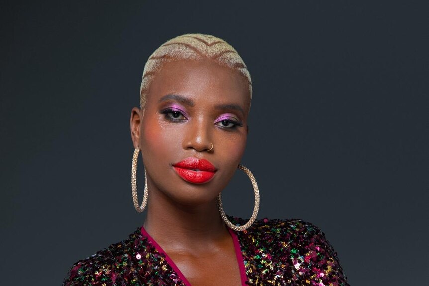 A photo of Khadija wearing hoop earnings, short bleached hair and red lipstick. 