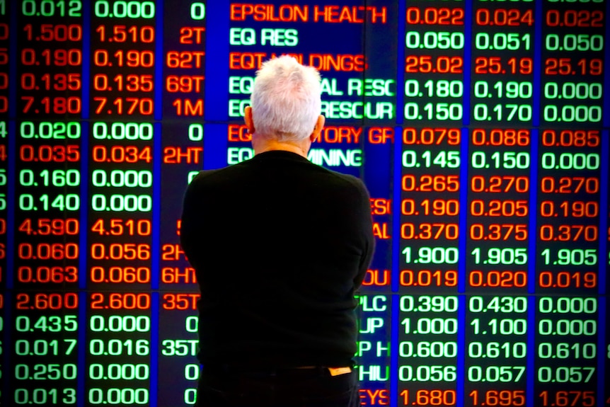 A stock market watcher stands in front of an ASX board.