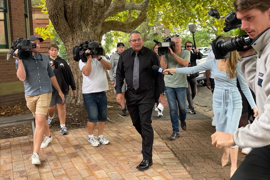 A man walking into a court surrounded by a media pack