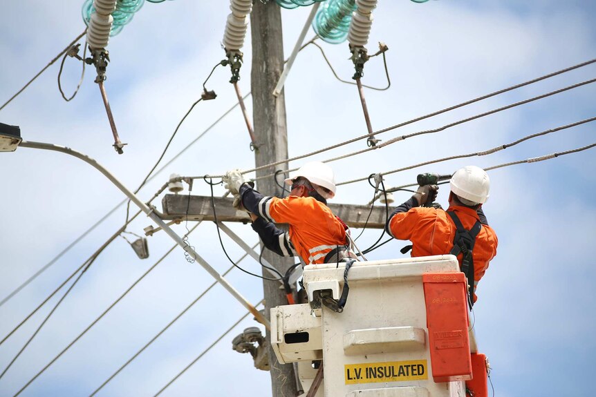 Two power workers in a cherry picker work to repair a power pole.