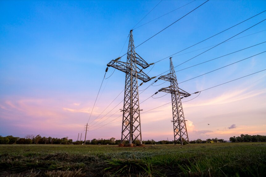 Two power transmission towers in the middle on an open field with a sunrise in the background., 