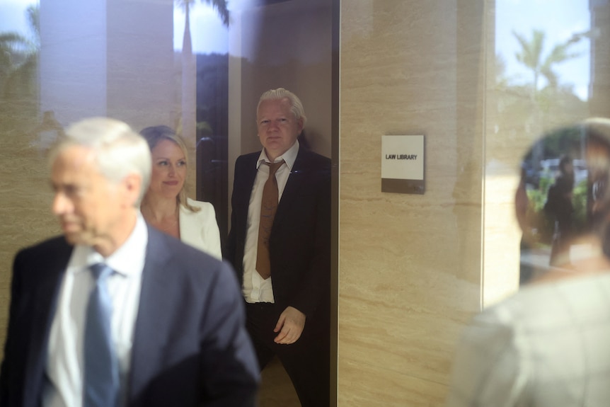 A blurry photo of a man and woman walking through a door frame. with others in the foreground.