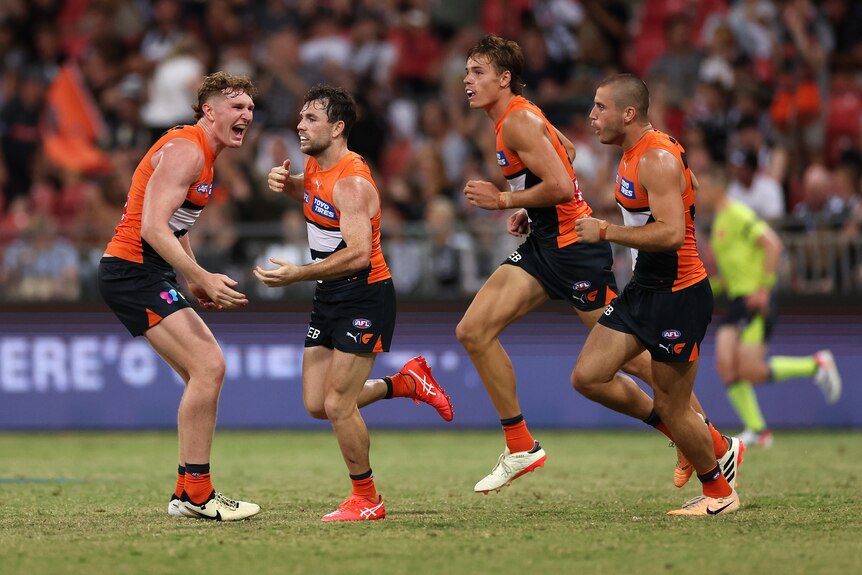 A group of Giants AFL players grin as they run back to the middle after a goal.