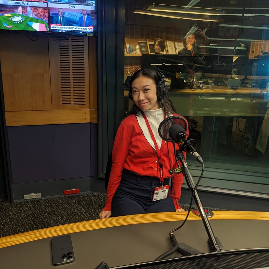 A woman in a red cardigan and white button down shirt behind the desk in the RN Radio studio.