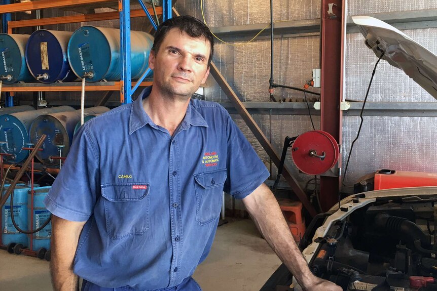 Acting Mayor Camilo Blanco in a mechanic's work shirt standing next to a car with an open bonnet.