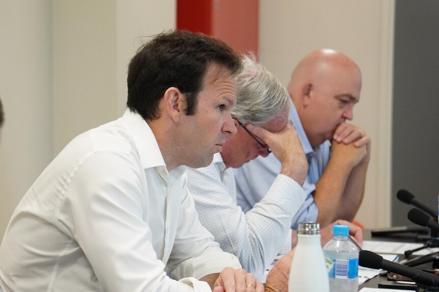 Three men in business shirts sit at a table.