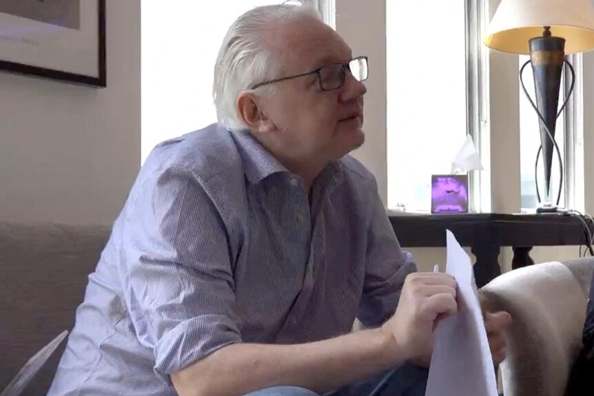 A man sits on a couch and holds papers.