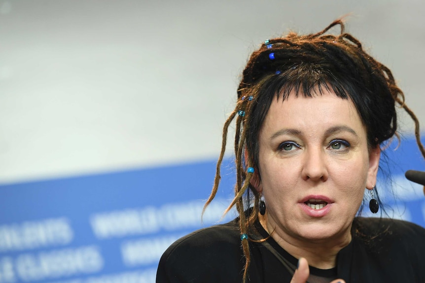 A close up of Olga Tokarczuk, with dreads and blue beads in her hair, talking at a panel