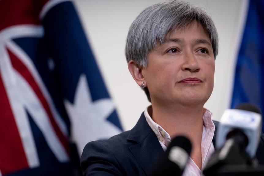 Penny Wong at a press conference standing in front of an Australian flag. 