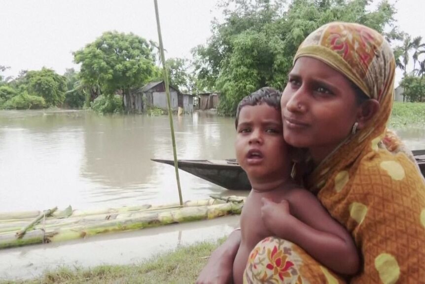 A woman holds a small boy with floodwaters in a field behind them.