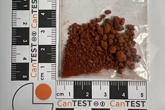A brown granular powder in a plastic bag beside a ruler. 