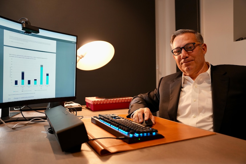 A Caucasian man in a business suit, sitting at his desk in front of a computer.