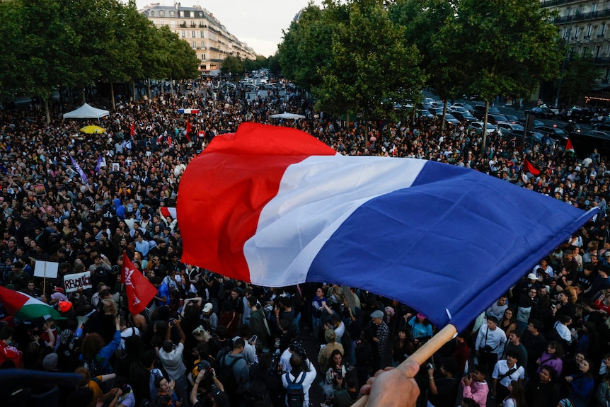 A red, white and blue flag is held amongst a large group of people.