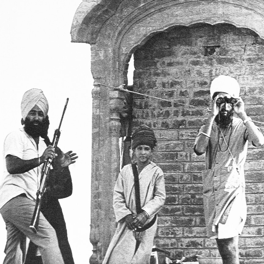A black and white photo of two men, one holding a rifle the other using binoculars, and a boy outside with near an ornate wall.