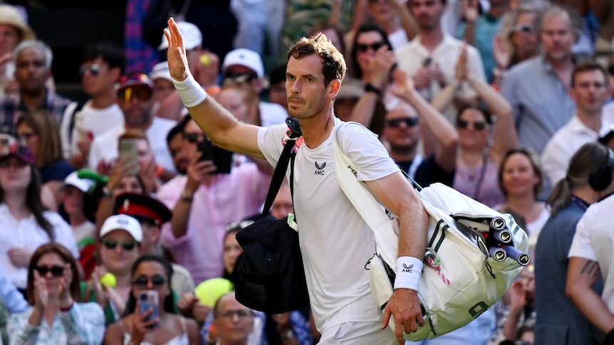 Tennis player Andy Murray walks off the court at Wimbledon carrying his bags and waving to the crowd.