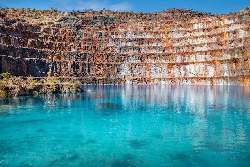 The red earth corrugations of an old mine pit surround a beautiful blue lake at the bottom.