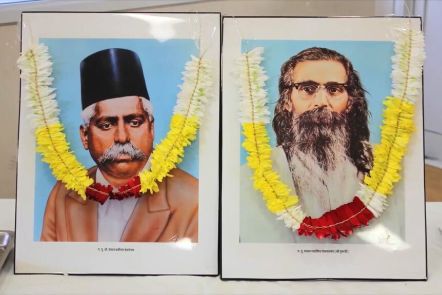 Two framed portraits of men, they are adorned with garlands. One man has long hair and a beard.