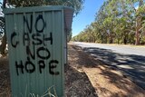 'No cash no hope' spraypainted in black on a green metal shed next to a highway.