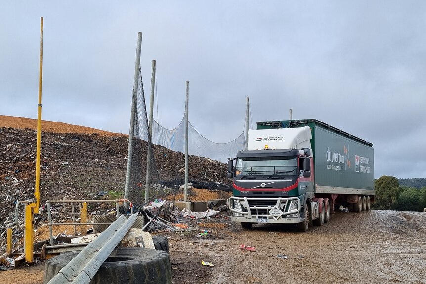 A truck parked on a gravel road beside a fenced off area containing refuse