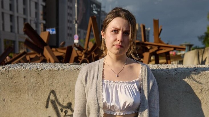 A woman stands in front of a wall in Kyiv. Behind the wall there appears to be a timber baricade