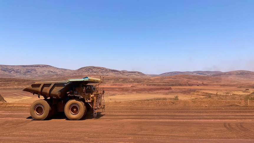 A dump truck drives along red dirt near a mine