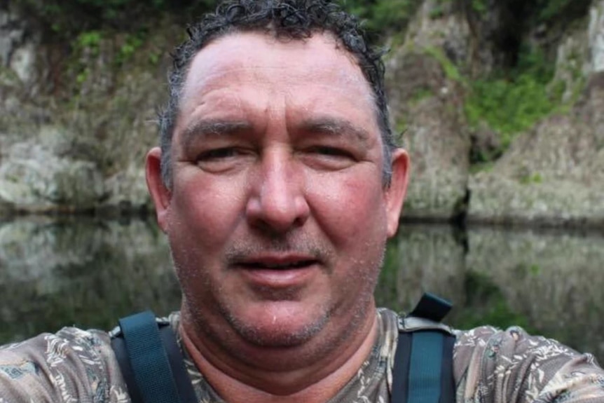 A close up of Greg Lynn standing in front of a body of water near some rocks.  