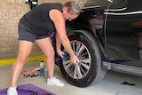A woman in shorts holds a wrench to a tyre.