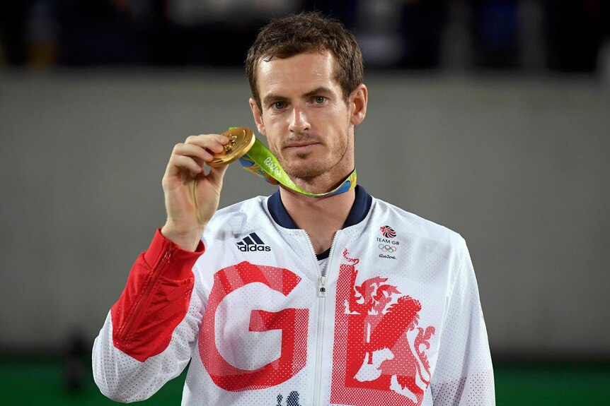 Great Britain tennis star Andy Murray stands wearing a "GB" top, holding an Olympic gold medal.  