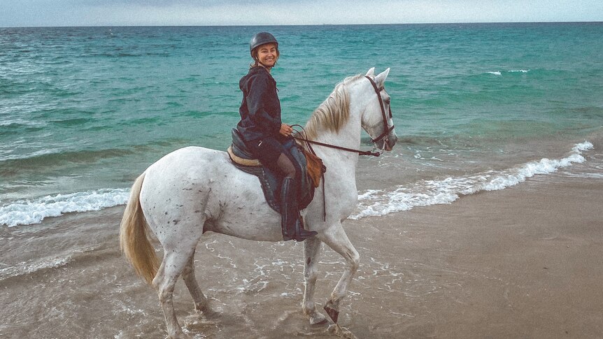 A lady riding a white horse on a beach