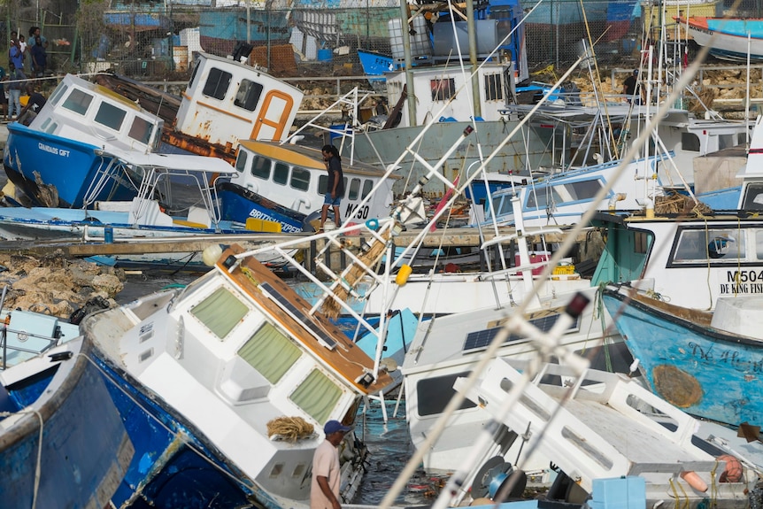 A man in a pink shirts walks in front of blue and white boats tilted in all directions.