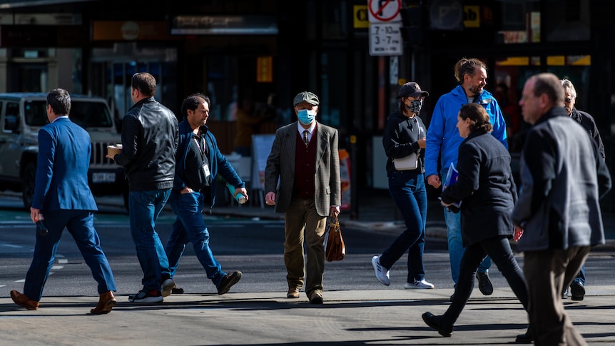 行人从各个不同方向穿过一条城市道路。一名走向镜头的男子戴着一个蓝色的外科口罩