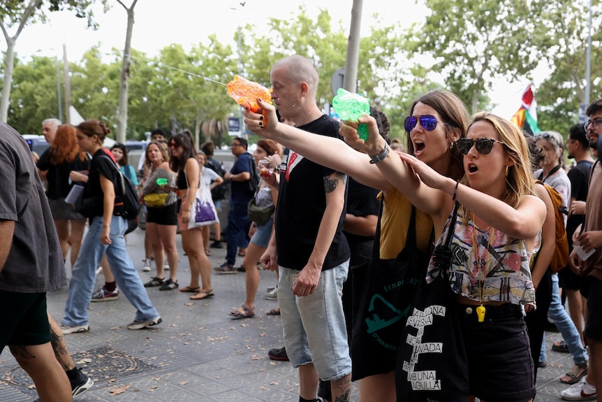 Two young women stand in a crowd of protesters shouting and shoot plastic water guns