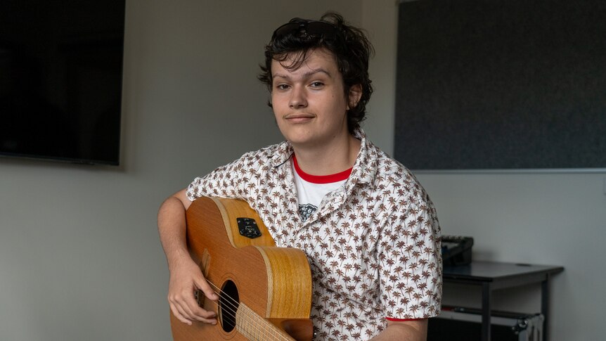 a young man holding an acoustic guitar smiles at the camera