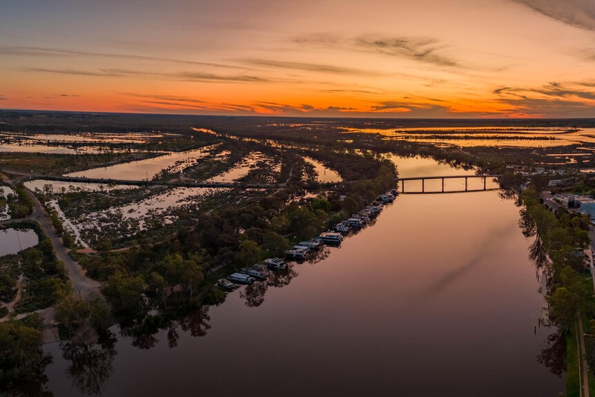 A wide sweeping river with an orange sunset,  a bridge across the narrow part. 