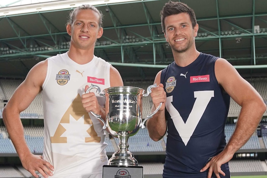 Nat Fyfe and Trent Cotchin smile while holding a big silver trophy between them.