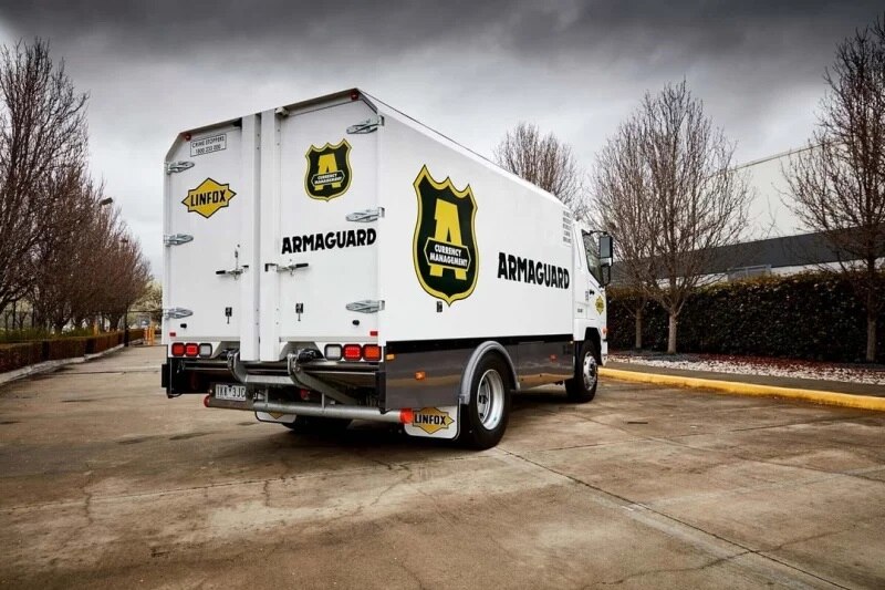 A white van carrying Armaguard's badge logo stationary in a parking lot.