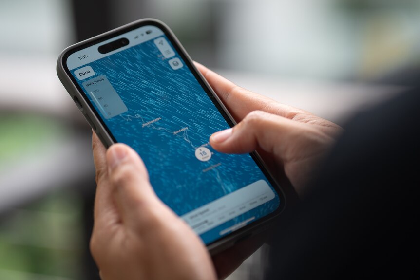 A phone held in tow hands showing weather patterns on the screen.